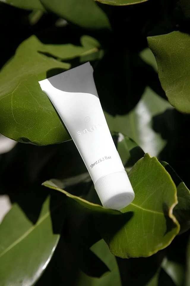 White Cosmetic Tube Surrounded by Leaves